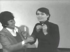 Still from a video of Sheila De Bretteville's November 1974 lecture. Shelley Kappe assisting her with her microphone.